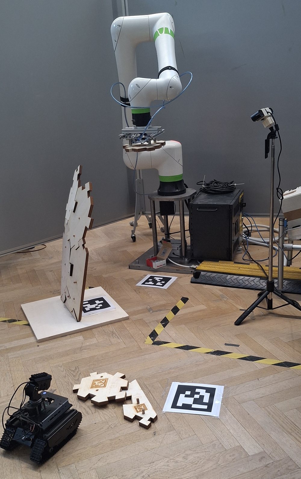The robot arm placing a plywood panel on the structure while the rover sits by the panel stack